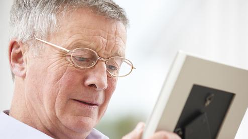 Ein älterer Mann mit Brille betrachtet ein Foto in einem Bilderrahmen.